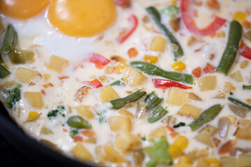 In a black pan, appetizer omelet fried eggs with fresh vegetables.