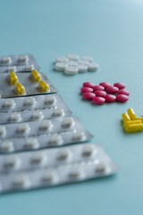 Blisters with tablets and capsules and three piles of multi-colored tablets sorted by color: white, pink, yellow. Medical concept on a blue background, treatment of diseases and viruses, pharmacy.