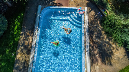 Active children in swimming pool aerial top view from above, happy kids swim on inflatable ring donuts and have fun in water on family holiday vacation on resort
