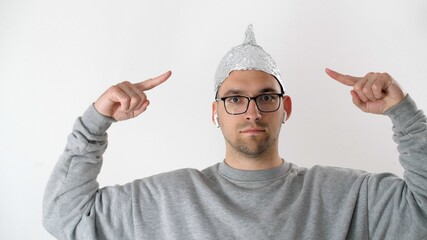 White serious attractive man in a foil hat points his fingers at the tinfoil hat. 5G tower...