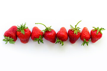 Line of ripe, red, fresh strawberries with elevated green tails on white background. Summer tasty fruit. Organic food. Copy space