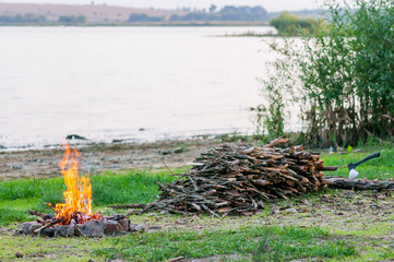 Small campfire with flames beside a lake with wood pile on the side.