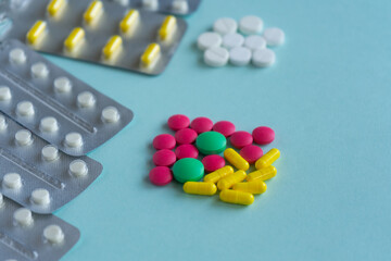 A handful of multi-colored tablets and blisters on a blue background. Pink, yellow, white and green pills of various shapes. Medical concept, treatment of diseases and viruses, pharmacy, healthcare.
