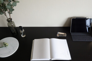 Top view of working corner decorated with laptop, white candles and artificial plant in glass vase on black wood  working table with beige painted wall in the background /copy space