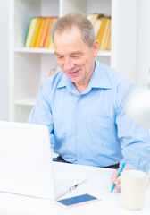 Fototapeta premium Handsome elderly man with a smile works at the computer in the office