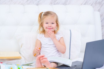 Girl with a smile is engaged while sitting on her bed using a laptop
