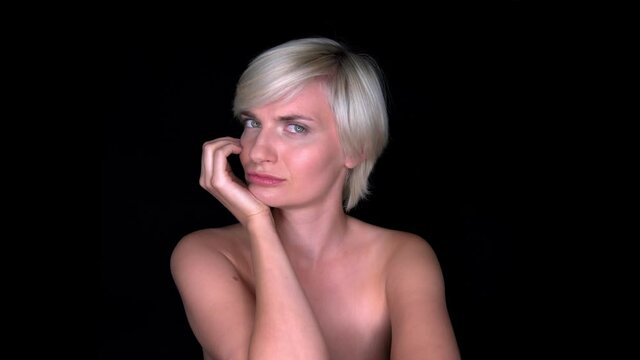 Blond-haired temptress. Sexy naked woman smiling mysteriously on a black background. Her beautiful fair skin and blue eyes shine in the light. The Temptress seduces a man.