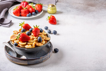 Pancake cereal. Heap of  mini pancakes  in gray bowl served with berries on concrete background.  Trendy food.