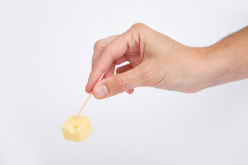 Hand holding diced cheese with toothpick isolated on white background. Studio shot. Side view....