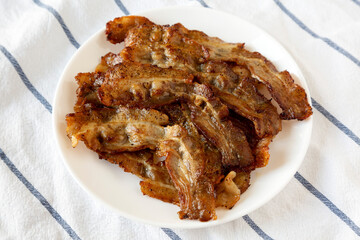 Homemade Fried Bacon on a white plate, low angle view. Close-up.