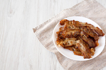 Homemade Fried Bacon on a white plate on a white wooden background, low angle view. Copy space.