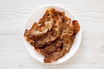 Homemade Fried Bacon on a white plate on a white wooden table, top view. Overhead, from above, flat lay.