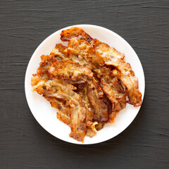 Homemade Fried Bacon on a white plate on a black background, top view. Overhead, from above, flat lay.