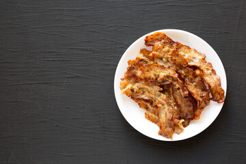 Homemade Fried Bacon on a white plate on a black surface, top view. Overhead, from above, flat lay. Space for text.