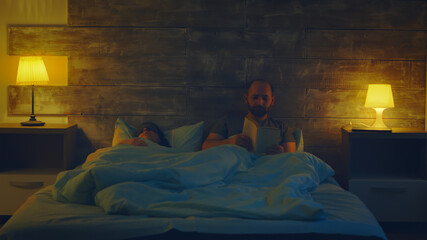 Beautiful wife saying good night to her husband while he's reading a book.