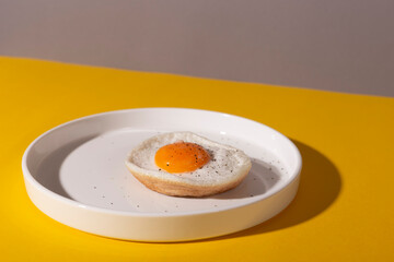 Fried egg on a white plate on a yellow background with shadows.