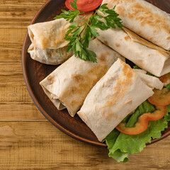Hot pita bread wrapped with cheese and vegetables and greens on a rustic plate.
