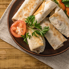 Hot pita bread wrapped with cheese and vegetables and greens on a rustic plate.