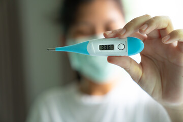 A women nurse holding a digital thermometer which indicates high temperature. Medical concept of corona virus outbreak.