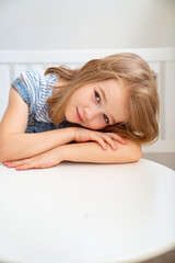 Fototapeta premium Little girl in denim sits on white bench at table. bright workplace for child