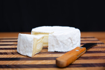 Soft cheese and knife laying on wooden board. Delicious brie cheese. Studio shot. Selective focus. Side view. Dairy meal and cooking on quarantine concept for flyers and banners