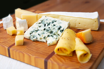 Blue, soft and hard cheeses laying on wooden board. Blue cheese, brie, camembert. Studio shot. Selective focus. Side view. Dairy meal and cooking on isolation concept for flyers and banners