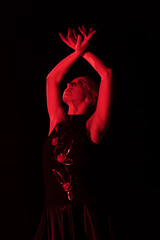 red lighting on young woman with hands above head dancing flamenco isolated on black