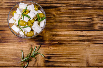 Fototapeta na wymiar Chopped feta cheese, rosemary and olives in glass bowl on a wooden table. Top view