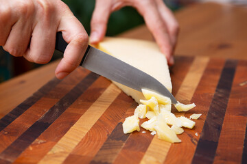 Female hands cutting parmesan on wooden board. Delicious cheese for breakfast. Studio shot. Selective focus. Side view. Dairy meal and cooking on isolation concept for flyers and banners