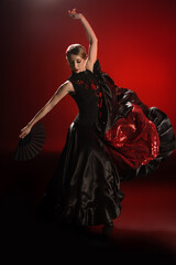 pretty flamenco dancer in dress holding fan while dancing on red