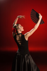 young flamenco dancer in dress looking at fan on red