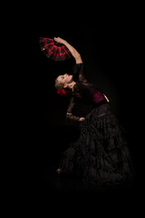 young flamenco dancer with hand on hip holding fan and dancing isolated on black - obrazy, fototapety, plakaty