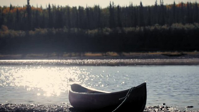Yukon River, Yukon Territories, Alaska. Metalic canoe on a pebble beach in the sunset with the forest in teh other side of the river. Yukon River.
