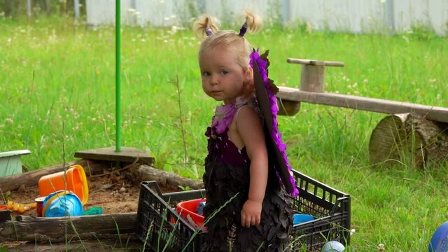 Little cute blond girl with butterfly wings plays near the vilage sandbox