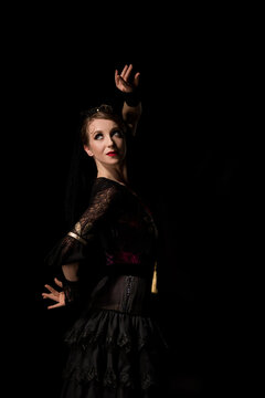 elegant flamenco dancer looking away and dancing isolated on black