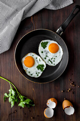 Fried eggs on frying pan on wooden table top-down