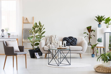 Stylish coffee table in the middle of spacious living room interior with white sofa, urban jungle and grey chair