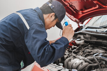Asian Man mechanic inspection Shine a torch car engine checking bug in engine.Blue car for service maintenance insurance with car engine.for transport automobile automotive