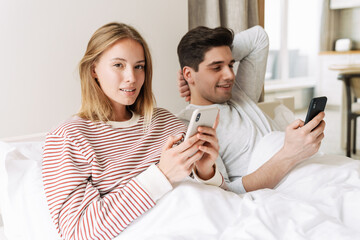 Portrait of happy couple smiling and using smartphones while lying