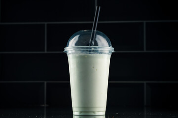 vanilla milkshake in plastic glass on a dark background. vanilla milkshake in takeaway cup