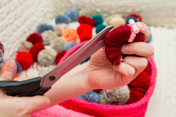A girl cuts a handmade pompom with scissors. The process of making pompons from threads