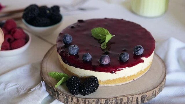 The man decorates with blueberries a cheesecake with raspberry and speckles on a wooden board