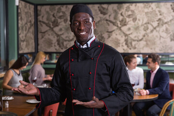 Smiling politely African American chef inviting to visit cozy restaurant