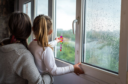 mother and daughter look out the window in rainy weather