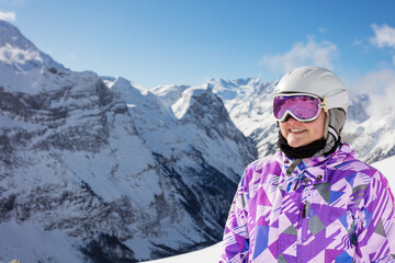 Close portrait of happy teen girl smile wear cute winter ski outfit glasses, helmet over mountain peaks