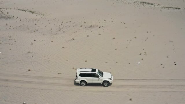 A white suv driving fast, through a desert race track, drone circle