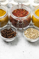 Spices and condiments in glass jars on a light gray table. Spices close-up with space for text