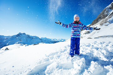 Cute beautiful young girl in vivid blue ski outfit throw snow in the air over mountain and sky