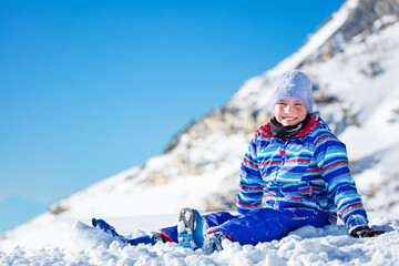Happy little girl sit in the snow with big smile in winter coat and hat