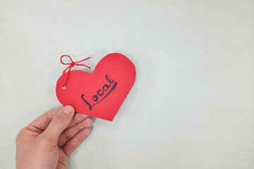 Human hands holding a red heart tag with handwritten word local. Promote, support, buy, shop and love local business concept. Gray background.